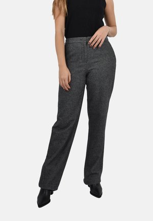 Donna che indossa pantaloni a vita alta grigio carbone a gamba larga, top senza maniche neri e stivali neri a punta su sfondo bianco.