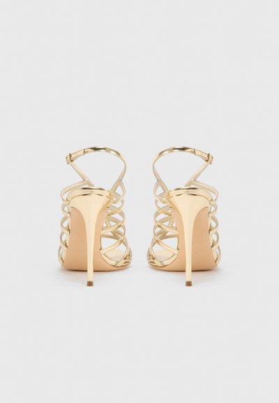 Χρυσά ψηλοτάκουνα σανδάλια με λουράκια που διασταυρώνονται, ανοιχτή πλάτη και λεπτά τακούνια στιλέτο. Λείο μεταλλικό υλικό με μινιμαλιστικό σχέδιο.
