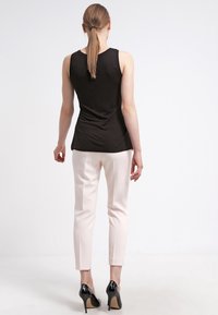 Zwarte mouwloze top gecombineerd met lichtroze getailleerde broek en zwarte hoge hakken. De top heeft een gladde textuur, terwijl de broek op maat is gemaakt.