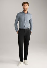 Kariertes Hemd mit einem blau-weißen geometrischen Muster, kombiniert mit schwarzen Hosen und weißen Sneakers. Glatte Textur, taillierte Passform.