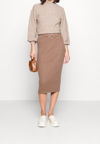 Brun stickad tröja med ballongärmar tillsammans med en ribbad brun knälång kjol med dekorativt bälte och beigea slip-on skor.