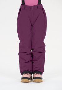 Lila Schneehosen mit verstellbaren Trägern, glatter Oberfläche, Fronttaschen und verstärkten Säumen. Tragen mit rosa und schwarzen Stiefeln.