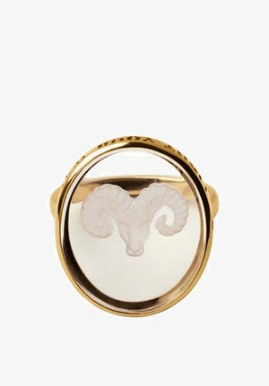 Anillo de oro con una cara redonda clara que presenta una cabeza de carnero blanca grabada con cuernos curvados en el centro.