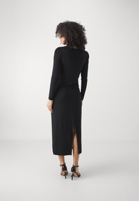 Must mustad dress, mille varrukatega, sobitatud kehaosaga, seljalt lõhiku, valmistatud pehmest materjalist. Kanda mustade kõrge kontsaga kingadega.
