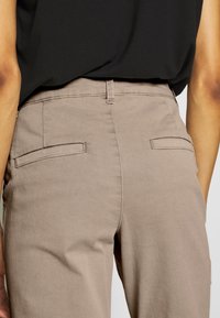 Beżowe spodnie z mieszanki bawełny o gładkiej fakturze, z dwoma tylnymi kieszeniami i prostym krojem. Pas jest gładki, bez widocznych zapięć.