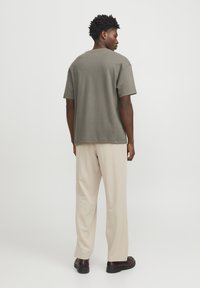 Kortærmet, olivengrøn t-shirt med afslappet pasform og rund halslinje, parret med beige bukser og brune sko, set fra ryggen.