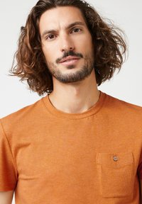 Oranje T-shirt met korte mouwen, gemaakt van gestructureerde stof, met een linker borstzak met een knoopdetail. Ronde hals en casual pasvorm.