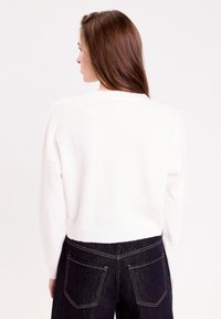 Pull blanc et doux avec un col rond et des manches longues, associé à un jean en denim foncé avec des coutures de poches et une coupe ajustée.