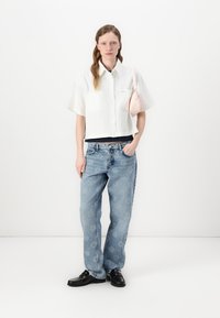 White short-sleeved shirt, blue high-waisted jeans, black lace-up shoes, and a small pink handbag. Smooth fabric with a casual fit.