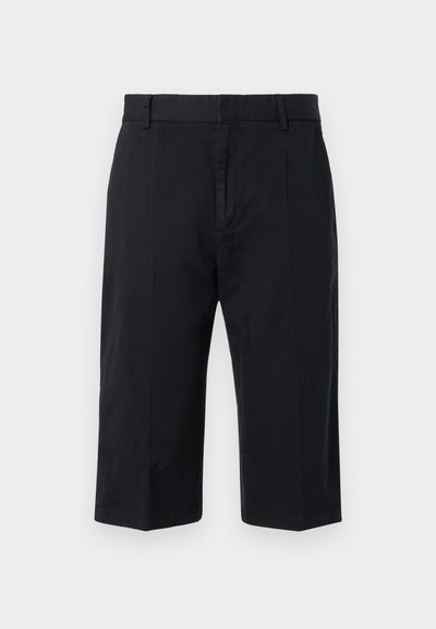 Shorts noirs arrivant au genou en coton, avec une coupe à plat, des passants de ceinture et sans poches visibles. Texture lisse et coupe ajustée.