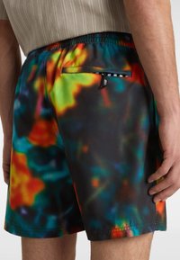 Bunte Badeshorts in Schwarz mit einem mehrfarbigen abstrakten Muster. Mit elastischem Bündchen und einer mit Reißverschluss versehenen Gesäßtasche.
