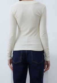 Langärmliges, geripptes Oberteil in hellem Creme mit Rundhalsausschnitt, kombiniert mit dunkelblauen, hoch taillierten Jeans mit Gesäßtaschen und sichtbaren Nähten.
