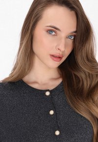 Zwart textuur top met een ronde halslijn en drie decoratieve knopen met crèmekleurige centra, omlijst door lang, golvend haar.