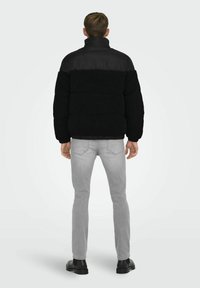 Chaleco de plumas negro y gris con textura suave, cuello alto y cintura elástica, combinado con jeans gris claro y botas negras.