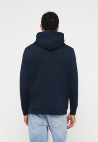 Navy blue hoodie made of soft fabric with a relaxed fit, featuring a large hood, ribbed cuffs, and hem, worn with light blue jeans.