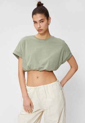 Cropped, short-sleeve shirt in light green cotton with a rounded neckline and gathered hem. Paired with cream-colored, drawstring trousers.