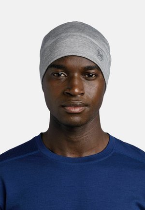 Graue Strickmütze mit glatter Textur und rundem Logopatch. Wird mit einem dunkelblauen Hemd getragen und zeigt ein einfaches, eng anliegendes Design.