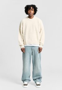 Cream textured sweater with dropped shoulders, paired with light blue baggy jeans and gray sneakers with white soles.
