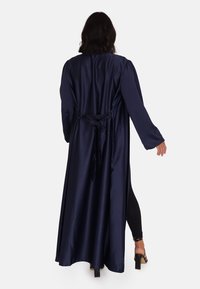Marinblå satinkappa med band i ryggen, långa ärmar och en flödande design; slät textur med en glänsande finish.