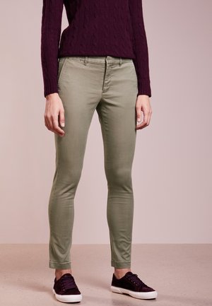 Osoba ubrana w oliwkowe dopasowane spodnie, ciemnofioletowy sweter warkoczowy i ciemnofioletowe trampki z białymi podeszwami.