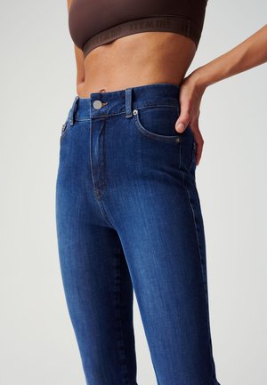 Hoge taille donkerblauwe denim jeans, met voorzakken, knoopsluiting en subtiele stiksels. Glad textuur en slanke pasvorm.