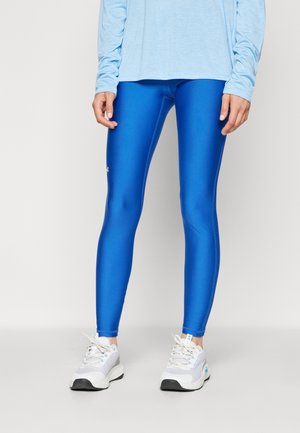 Leggings blu, lucidi, con una texture liscia e un design aderente, abbinati a una maglietta a maniche lunghe di un blu chiaro e scarpe da ginnastica grigie.