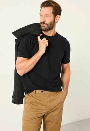 Schwarzes kurzärmliges T-Shirt aus Baumwolle, getragen unter einem dunkelgrauen Blazer. Beige Hose mit Knopfverschluss vervollständigt das Outfit.