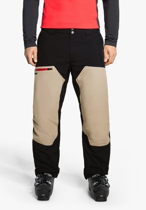 Schwarze und beige Skihosen mit einem körpernahen Schnitt, ausgestattet mit Kniefeldern, einer seitlichen Reißverschlusstasche mit roten Akzenten und verstärkten Säumen.