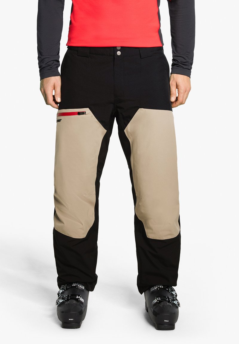 Black and beige ski pants with a fitted design, featuring knee panels, one zippered side pocket with red accents, and reinforced cuffs.