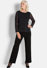 Top nero a maniche lunghe con maniche trasparenti, arricchito da glitter, abbinato a pantaloni neri a gamba larga e scarpe con tacco nere.