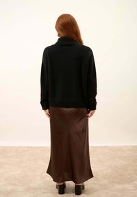 Czarny, oversize sweter z dzianiny z wysokim kołnierzem, zestawiony z dopasowaną, błyszczącą, długą brązową spódnicą. Gładka tekstura, prosty design.