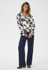 Tengeri virágmintás blúz elefántcsont színű virágokkal, puffos ujjal és kulcslyuk részlettel, navy széles szárú nadrággal és barna bokacsizmával párosítva.