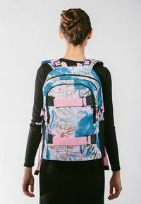 Barevný batoh s květinovým vzorem, s modrými a růžovými akcenty, nastavitelné popruhy a několik úložných přihrádek.