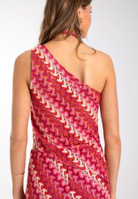 Vestido de un solo hombro con un patrón geométrico en rojo, rosa y crema. Fabricado con una tela ligera de textura suave y cintura elástica.