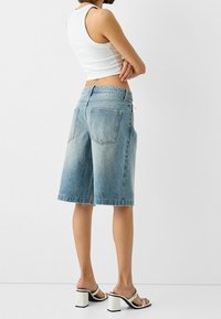 Ljusblå denimshorts i bermudastil med avslappnad passform, med midjeband, två bakfickor och fransad fåll. Bärs med vita klacksandaler.