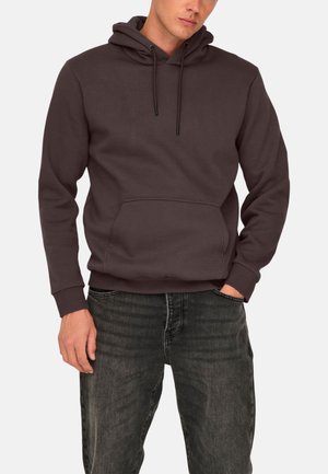 Dark brown hoodie made of soft fabric. Features a front pouch pocket, adjustable drawstring hood, and ribbed cuffs and hem. Jeans visible below.