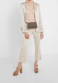 Blazer en satin rose clair, body en dentelle beige, pantalon large en satin crème, sac ceinture texturé marron, talons compensés roses avec découpes florales.