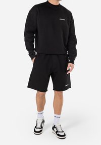 Black sweatshirt and matching shorts made of cotton blend, featuring a crew neck, elastic waistband, and a logo on the chest and shorts.