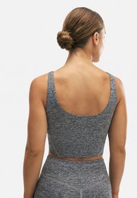 Sujetador deportivo ajustado en gris con una tela lisa y texturizada; tirantes anchos y un diseño de espalda baja. Adecuado para ropa de deporte.