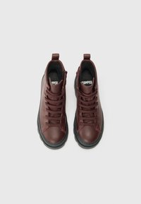 Bottes montantes en cuir bordeaux avec semelles en caoutchouc noir, design à lacets et col rembourré pour le confort. Présente la marque Camper sur la languette.