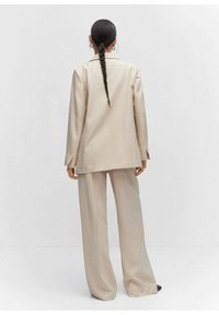 Veste de costume beige à fines rayures et pantalon à jambes larges. Le tissu a une texture lisse, avec des manches longues et une coupe décontractée. Design simple et ajusté.