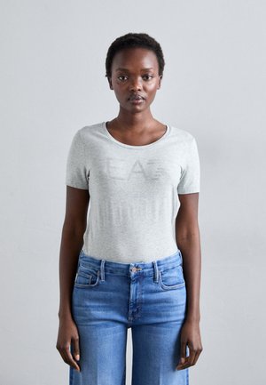 Lichtgrijs kortekruik t-shirt met een ronde hals, met het woord "EAZ" in een subtiele opdruk. Gecombineerd met hoge taille blauwe denim jeans.