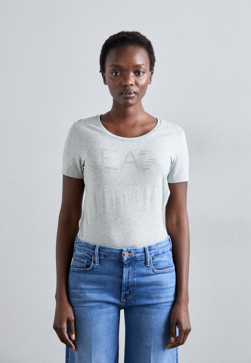 Tricou scurt din bumbac de culoare gri deschis, cu guler rotund, având un design subtil cu "EAZ". Asortat cu blugi din denim albastru cu talie înaltă.