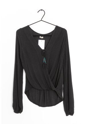Blusa nera a maniche lunghe con scollatura a V profonda, vita arricciata e lacci regolabili con frange. Realizzata in tessuto leggero e strutturato.