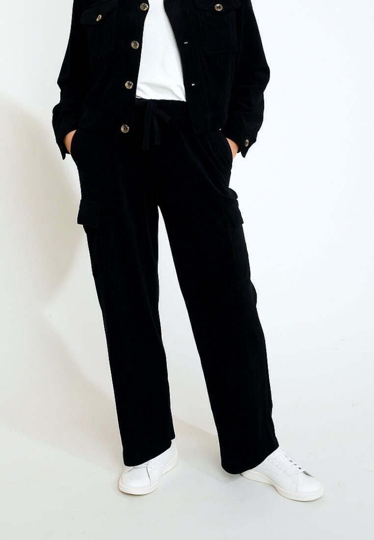 Schwarze Cordjacke mit Knopfverschluss und zwei Brusttaschen, kombiniert mit passenden Cargo-Hosen und weißen Sneakers. Glatte Textur.