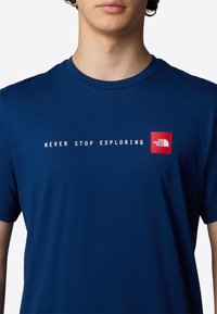 Camiseta de algodón azul marino de mangas cortas, con el texto blanco "NUNCA DEJES DE EXPLORAR" y un logotipo rojo en un cuadrado en el lado izquierdo del pecho.
