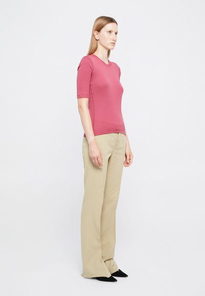 Rövid ujjú, testhez simuló felső világos rózsaszínben, bézs színű, bő szárú nadrággal párosítva. A ruházat egyszerű, letisztult kialakítású, sima textúrával.