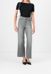 Top nero a maniche corte abbinato a jeans grigi a vita alta e gamba larga, con tacchi neri a punta. Borsa a spalla bianca completa il look.