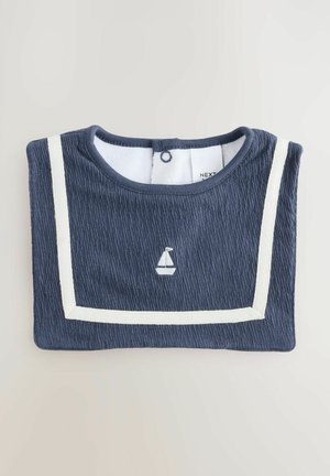 Tumesinine sööt koos tekstureeritud kangaga, millel on valged aktsendistribud ja paadi tikand. Tagaküljel nööbid, mis võimaldavad lihtsat selga panemist.