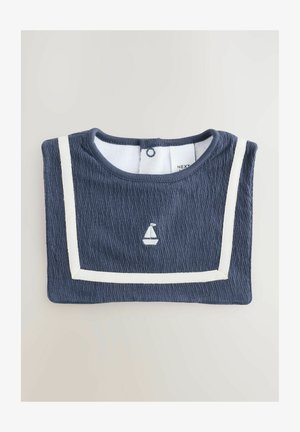 Tumesinine sööt koos tekstureeritud kangaga, millel on valged aktsendistribud ja paadi tikand. Tagaküljel nööbid, mis võimaldavad lihtsat selga panemist.